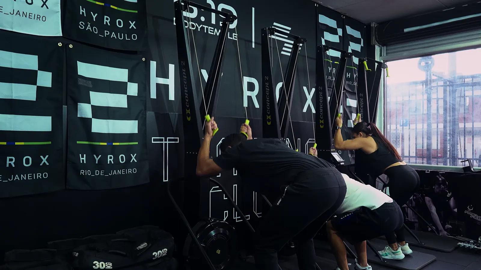 Atletas en los SkiErg frente a la pared Hyrox de BodyTemple